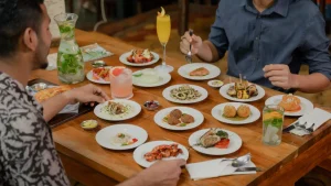 Multi cuisine food placed on a wooden table with guests enjoying in Mojigao Restaurant in Assagao North Goa