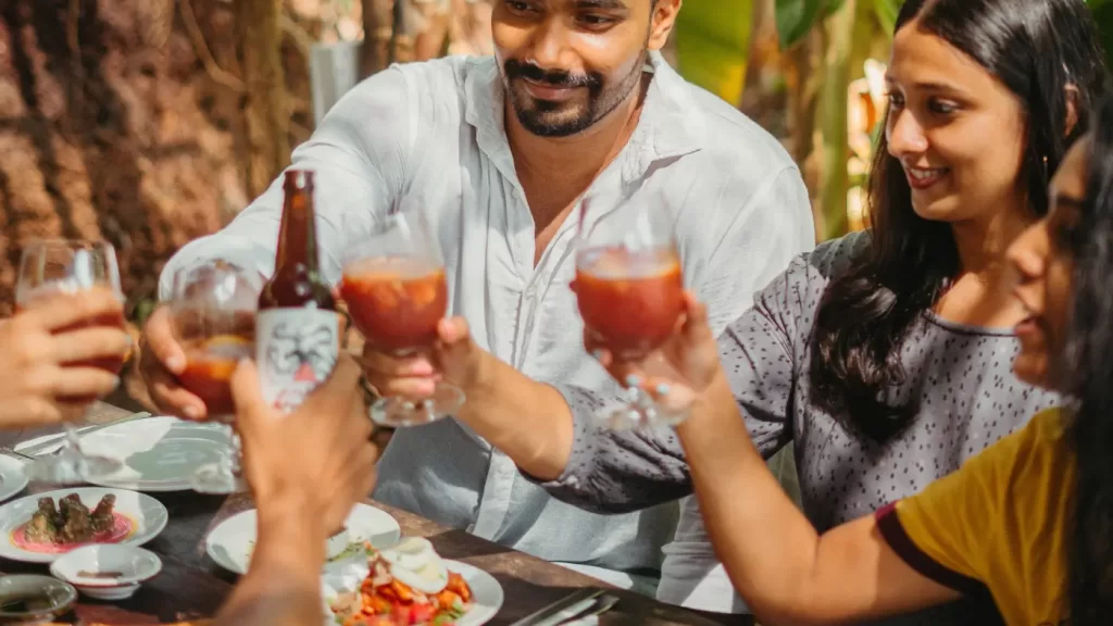 Friends clinking drinks at a sunny outdoor table, enjoying a cheerful meal together at Mojigao.