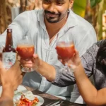 Friends clinking drinks at a sunny outdoor table, enjoying a cheerful meal together at Mojigao.