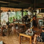 Vibrant Mojigao Restaurant scene with people at wooden tables, featuring warm lighting and lush greenery.