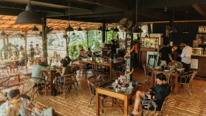 Vibrant Mojigao Restaurant scene with people at wooden tables, featuring warm lighting and lush greenery.